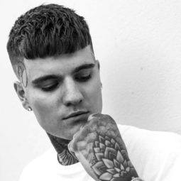 young men haircuts: black and white photo of a tattooed man with a textured french crop hairstyle