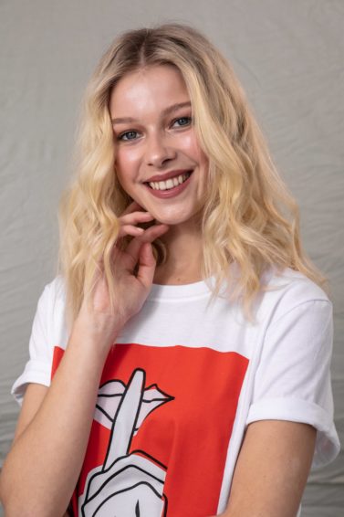 Volume hair: Blonde model with wavy tousled hair, wearing a white t-shirt with red design, touching her face with her hand