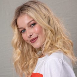 Woman with medium-length, golden blonde hair styled into textured waves, wearing a slogan top and posing in a studio setting