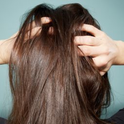 Itchy scalp causes: Back view of a woman with brunette straight hair with her hands in her hair