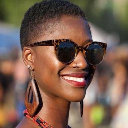 image of a black woman with very short natural hair smiling wearing sunglasses and wooden earrings